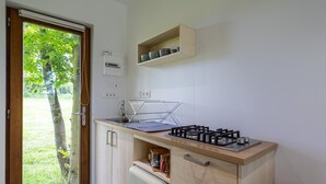 A compact kitchen with a gas stove, a small refrigerator, and a wooden cabinet. - Chalet 'La Cafoutche De Minus Renovated' with Private Terrace, Shared Garden & Wi-Fi (Gommenec'h)