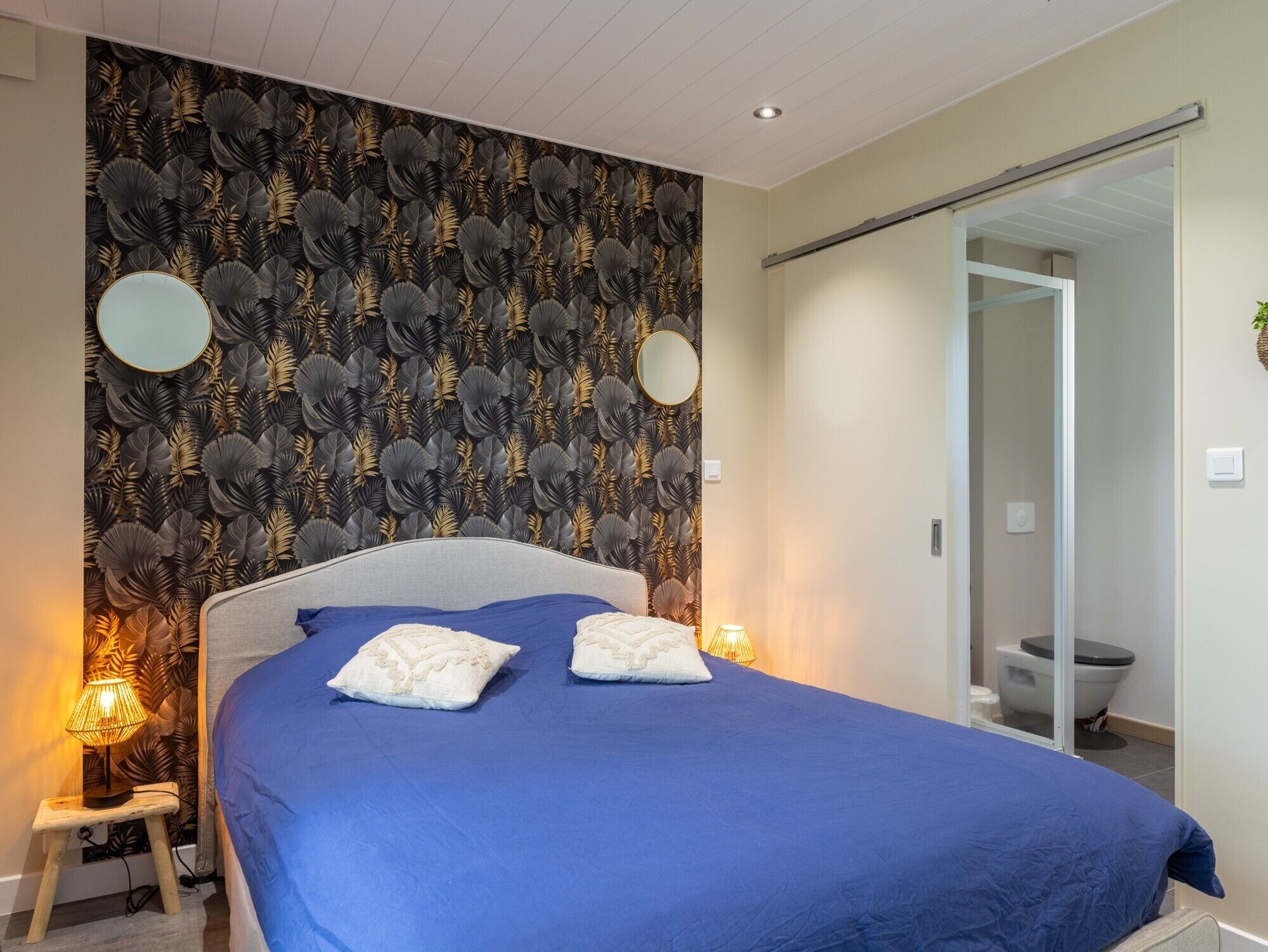 A bedroom with a bed, two bedside lamps, a mirror, and a sliding door leading to a bathroom.
