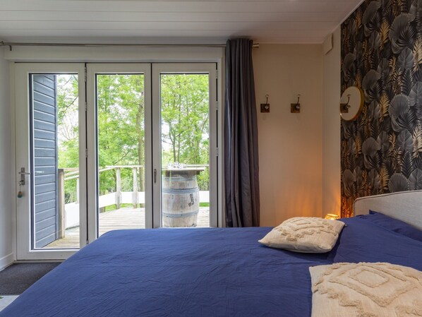 A bedroom with a large bed, a view through the sliding glass door, a wooden barrel outside, and a patterned wall.