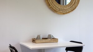 A white table with a wooden tray holding two pitchers, a woven mirror, and a black chair. - Chalet 'La Cafoutche De Minus Renovated' with Private Terrace, Shared Garden & Wi-Fi (Gommenec'h)