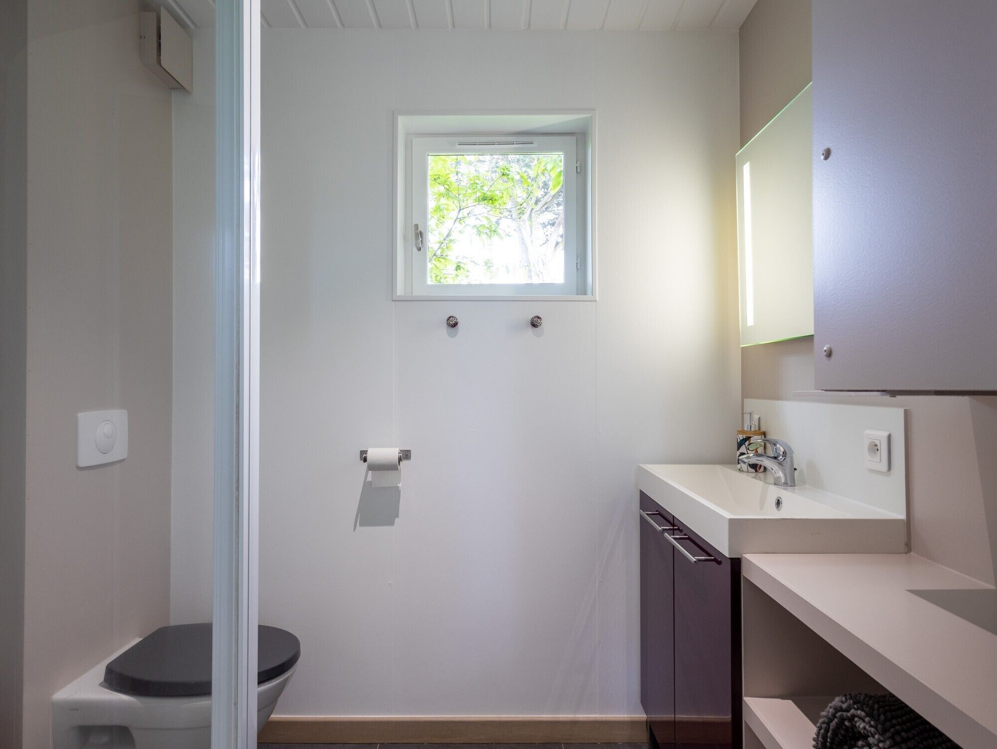 Ein kleines Badezimmer mit Toilette, Waschbecken, Spiegel und Fenster.