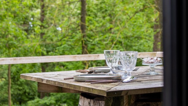 A wooden table set outdoors with clear glassware and plates, surrounded by a forested area. - Chalet 'La Cafoutche De Minus Renovated' with Private Terrace, Shared Garden & Wi-Fi (Gommenec'h)