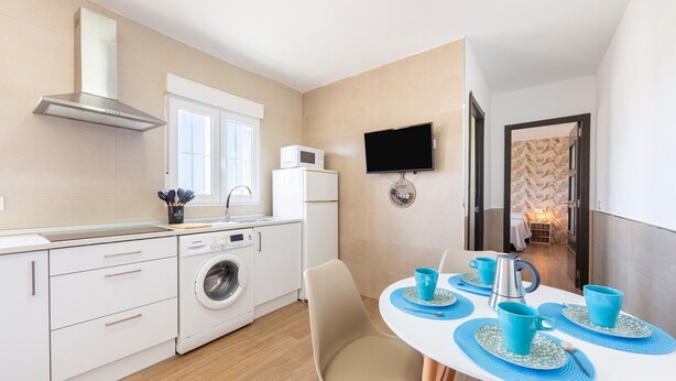 A modern kitchen with a microwave, washing machine, and a TV mounted on the wall.