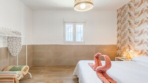 A hotel room with a bed, a hanging towel rack, a window, and a wall with a leaf pattern.