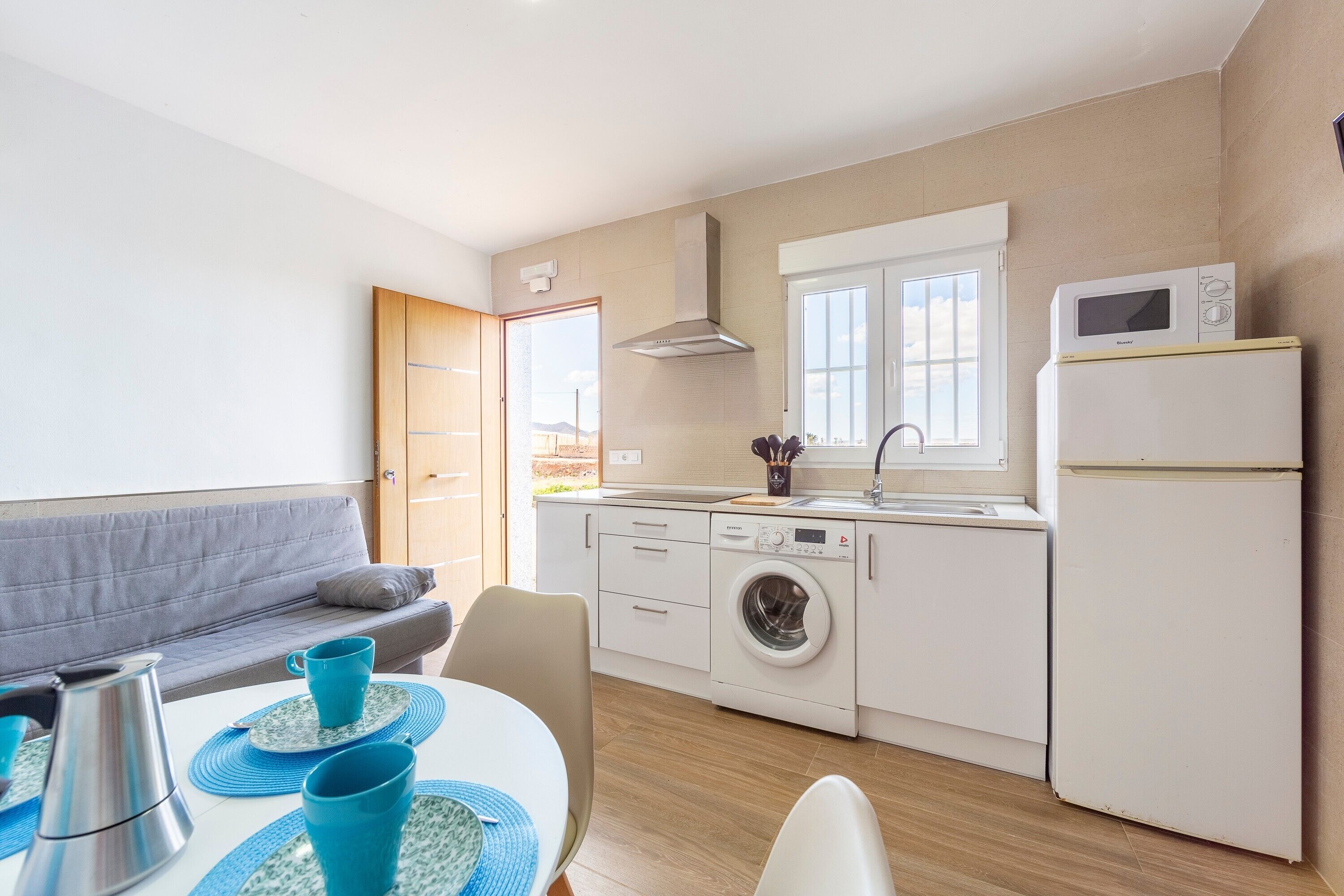A compact kitchen with a washing machine, microwave, and a dining area with a table and chairs.