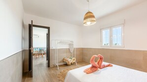 A bedroom with a bed, a towel rack, a window, and a door leading to another room.