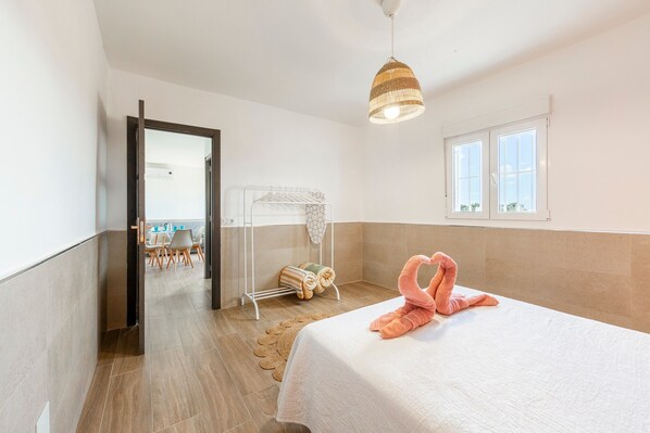 A bedroom with a bed, a towel rack, a window, and a door leading to another room.