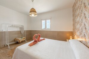 A bedroom with a bed, a hanging light fixture, a window, and a towel rack.
