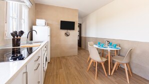A modern kitchen with a microwave, sink, and stove, a dining area with a table and chairs, and a flat-screen TV mounted on the wall.