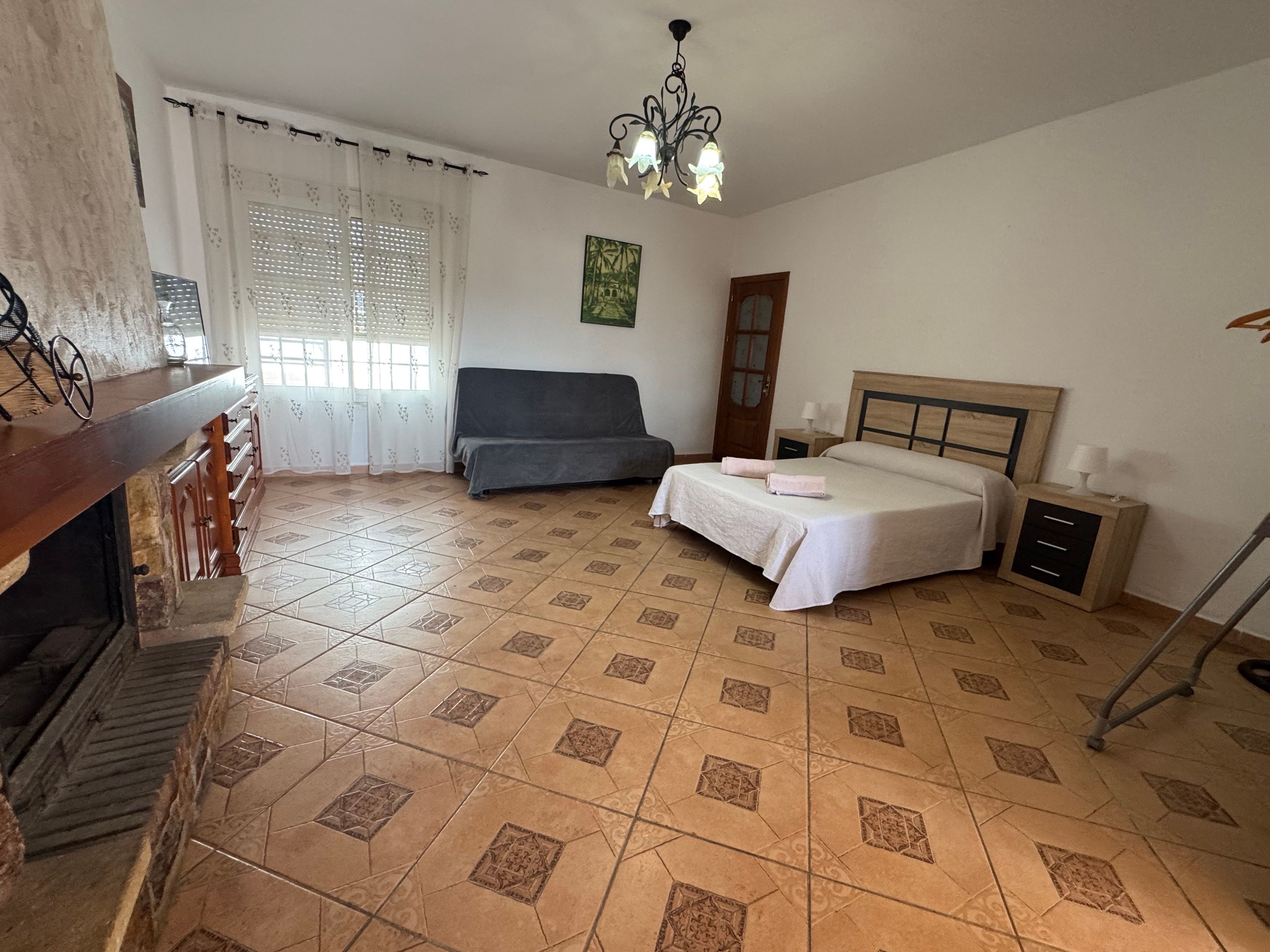 Una camera da letto con un letto, un comodino, una cassettiera, una finestra con tende, un lampadario e una scala.