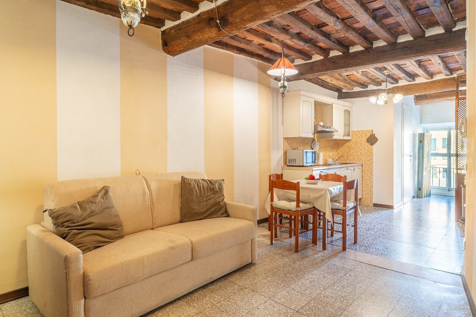 A living room with a sofa, a dining table with chairs, a kitchen area, and a hallway leading to an outdoor area.