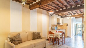 Ein Wohnzimmer mit einer Couch, einem Esstisch mit Stühlen, einer Küchenzeile und einem Flur, der zu einem Außenbereich führt.