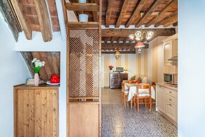 Une cuisine avec des meubles en bois, un coin repas avec une table et des chaises, et un plafond avec des poutres apparentes.
