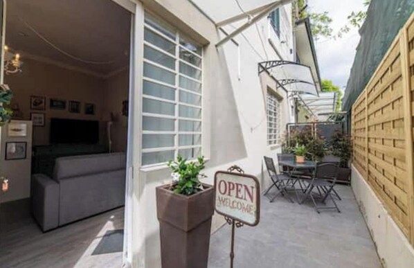 Un patio con un cartel que dice 'OPEN WELCOME', un conjunto de asientos y vista al espacio interior.