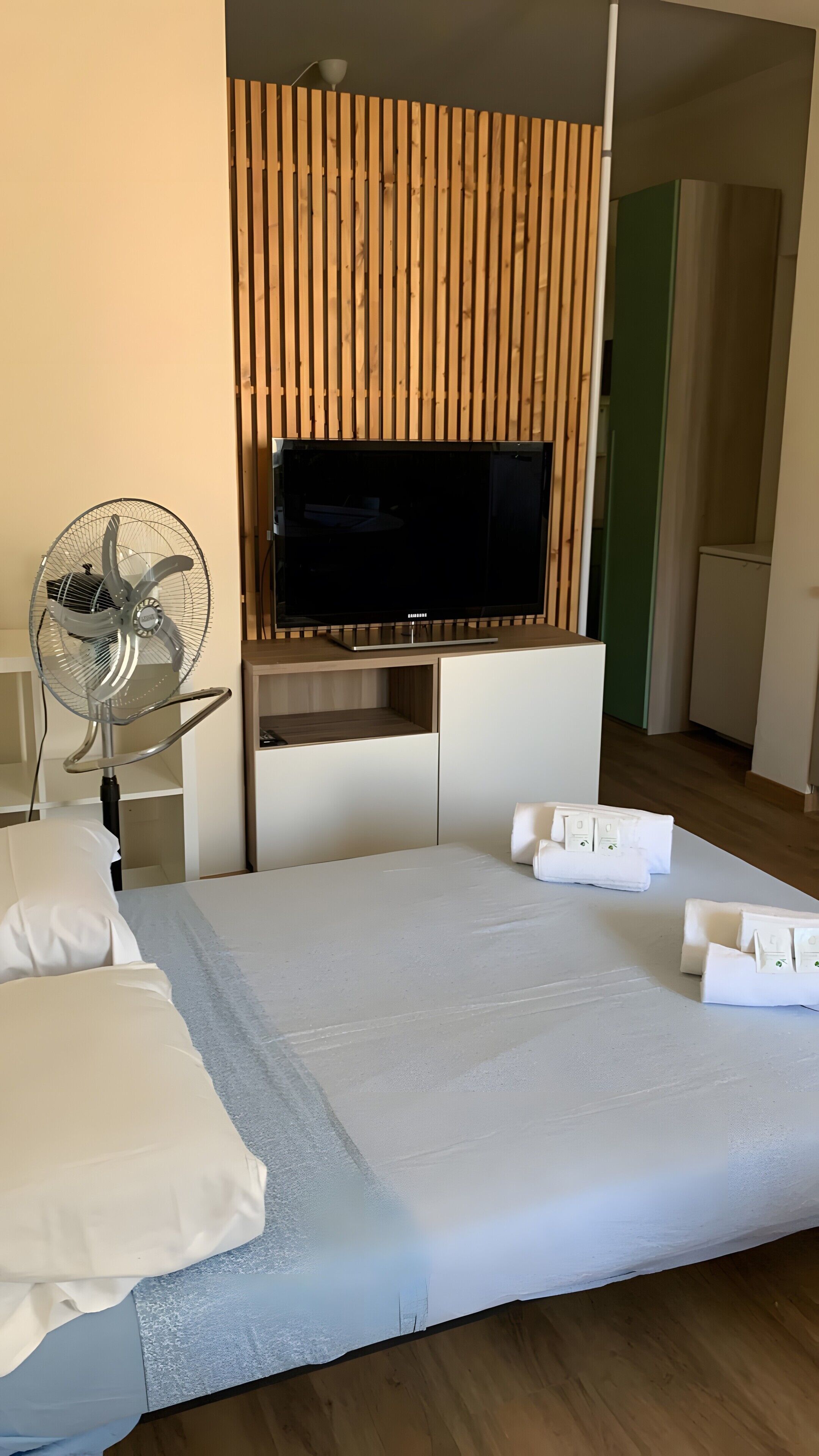 A hotel room with a bed, a TV, a fan, and a wooden panel wall.