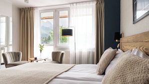 A hotel room with a large bed, two chairs, a small table with a plant, and a view of mountains through the window. - Hotel Rzemieślnik Zakopane  (Zakopane)