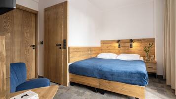 A hotel room with a wooden bed, a blue chair, a wooden wardrobe, and a small table with books.
