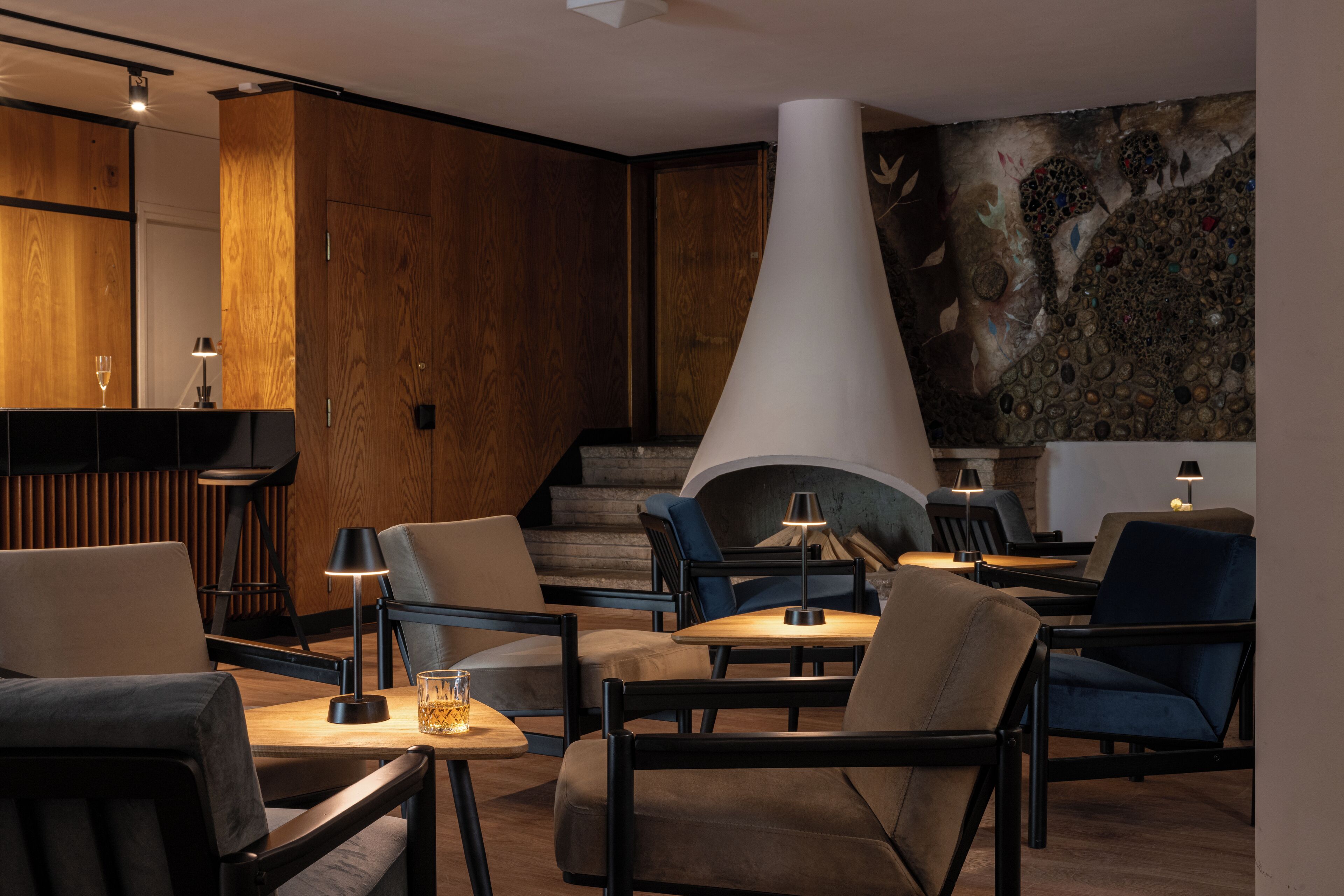 A modern lounge area with wooden paneling, comfortable seating, and a central fireplace.