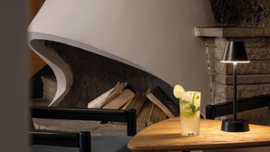 A modern interior with a curved white structure, a wooden table with a glass of drink, and a stone wall. - Hotel Rzemieślnik Zakopane  (Zakopane)