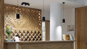A reception desk with a wooden finish and a chevron pattern, a large 'RECEPCJA' sign above, and a decorative wall with a lattice design. - Hotel Rzemieślnik Zakopane  (Zakopane)