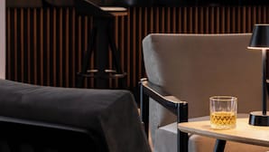 A bar area with wooden paneling, a glass display case with bottles, and a table with a glass and a lamp. - Hotel Rzemieślnik Zakopane  (Zakopane)