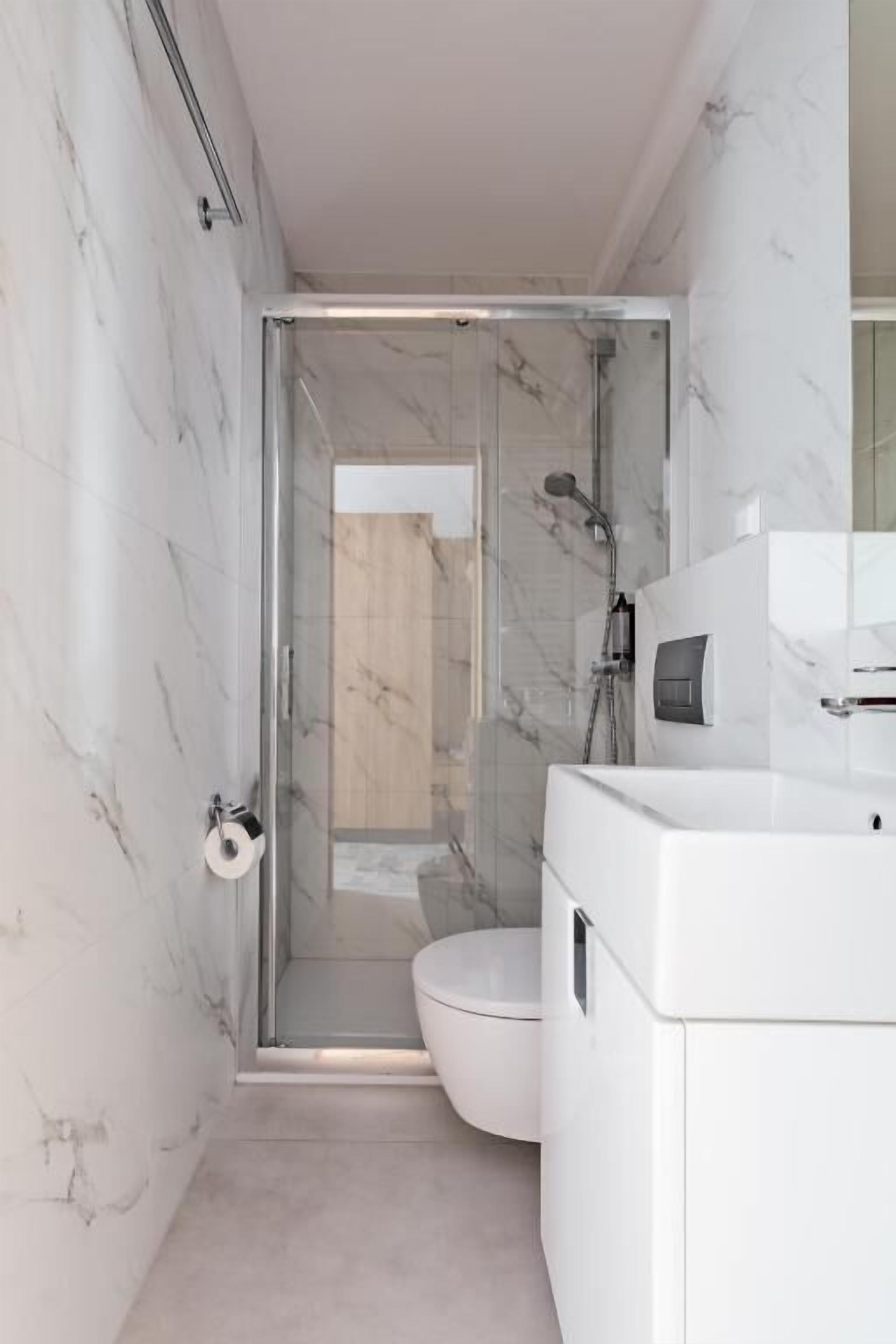 A modern bathroom with a glass-enclosed shower, a white toilet, and a marble wall.