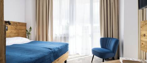 A hotel room with a bed, a chair, a table, and a TV.