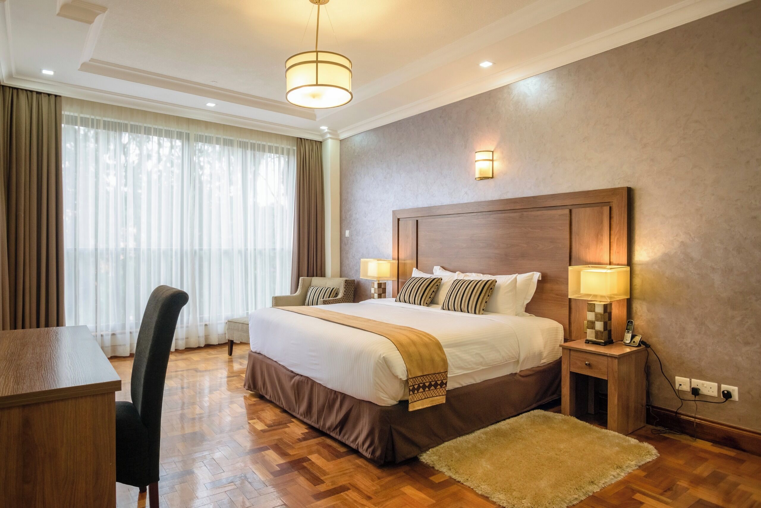 A hotel room with a large bed, bedside lamps, a desk, and a chair.