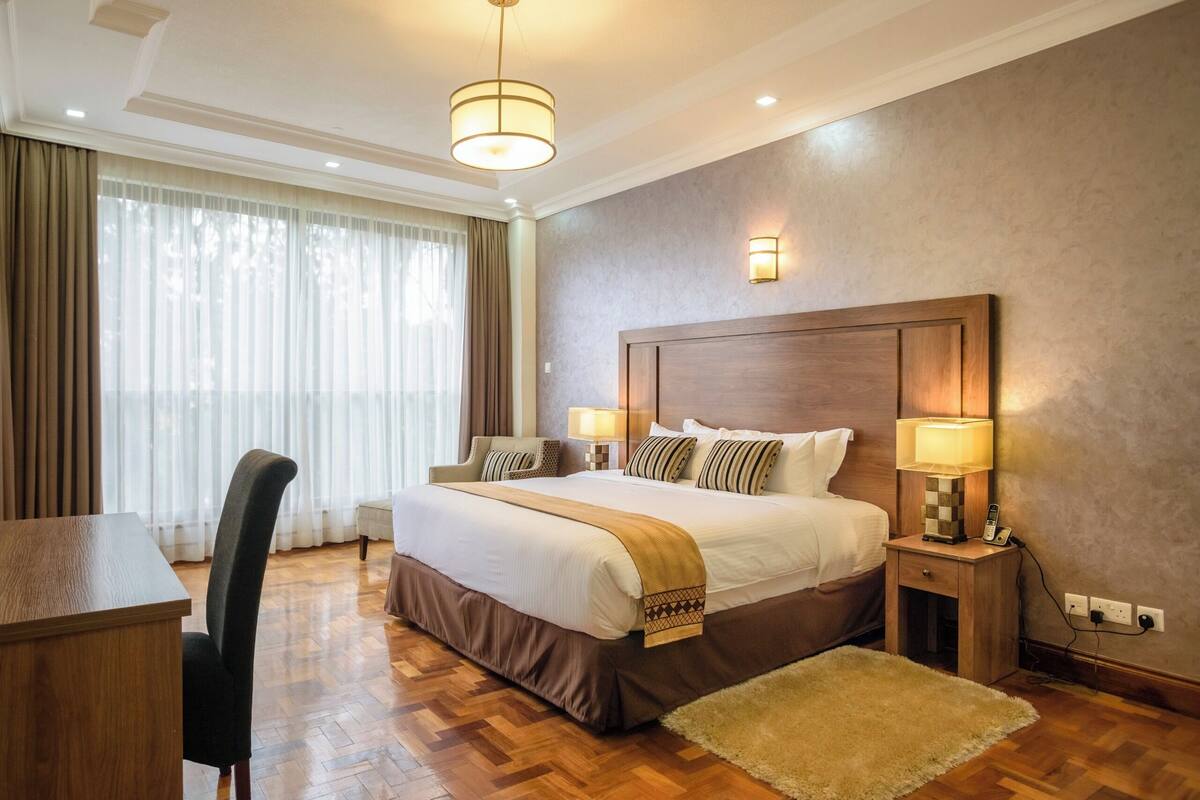 Una habitación de hotel con una cama grande, lámparas de noche, un escritorio y una silla.