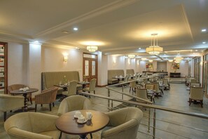 Un amplio vestíbulo de hotel con varias zonas de estar, incluyendo un salón con sillas a rayas y un comedor con mesas y sillas.