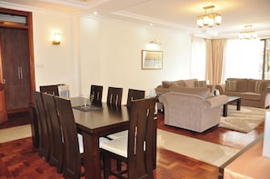 A dining area with a wooden table and chairs, a sofa, and a framed picture on the wall. - Gem Suites Hotel & Luxury Serviced Apartments (Nairobi)