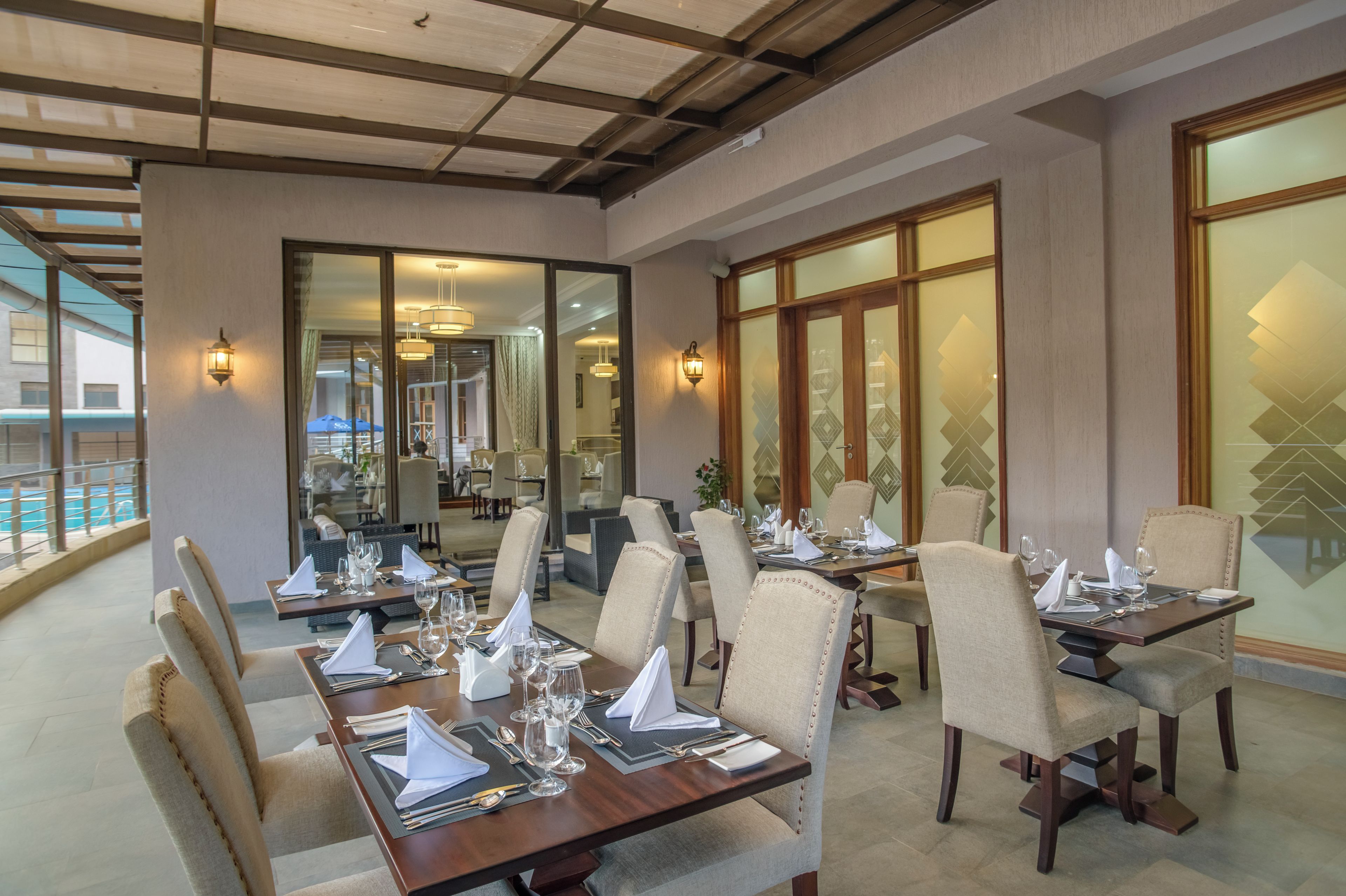 Uma sala de jantar com várias mesas preparadas para hóspedes, apresentando um design moderno com mesas de madeira e cadeiras estofadas.