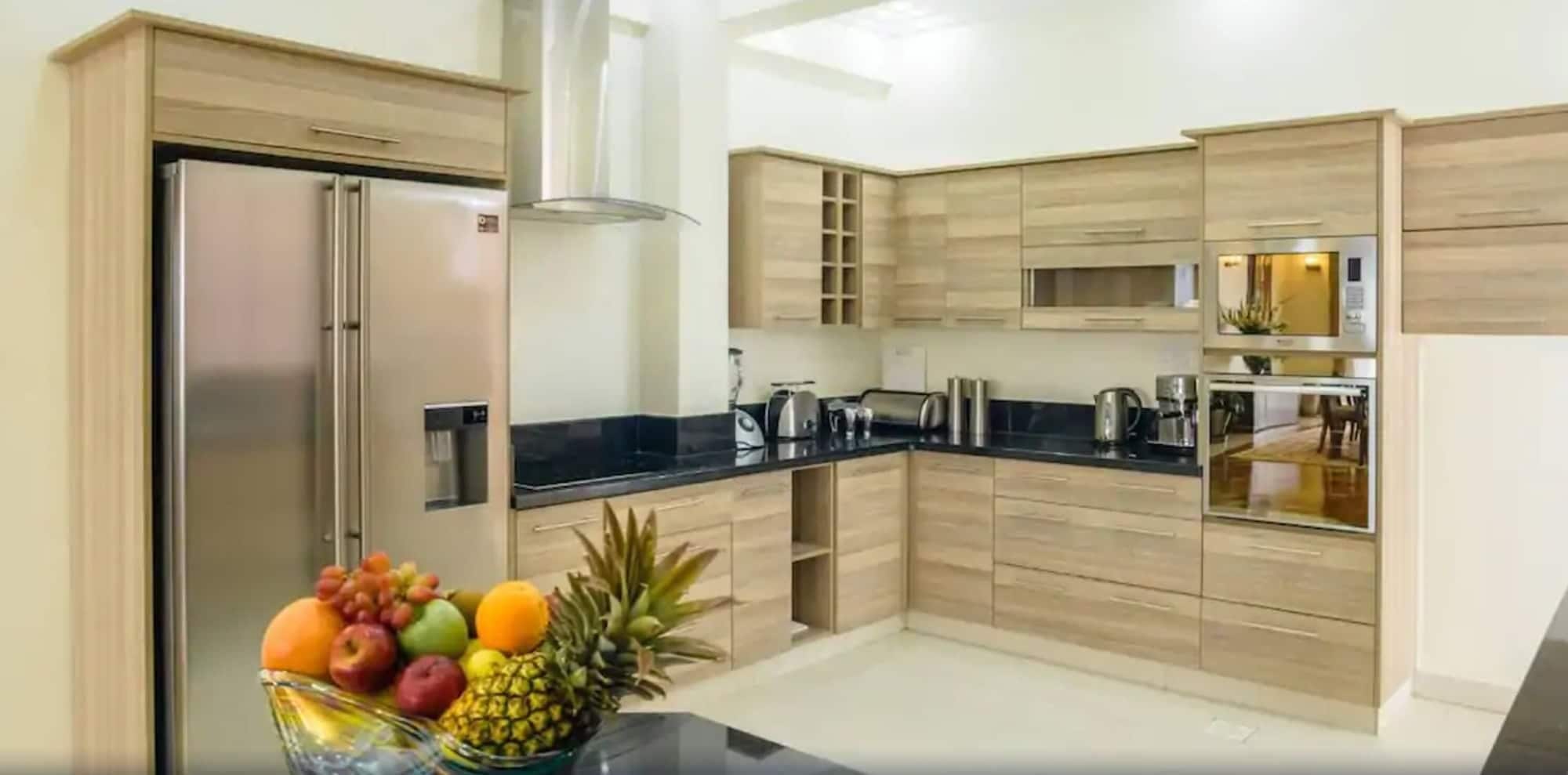 Cozinha moderna com armários de madeira, geladeira de aço inoxidável e bancada preta.