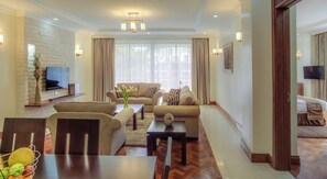 Una sala de estar moderna con un sofá, una mesa de centro, un televisor montado en una pared de ladrillo y una zona de comedor con una mesa y sillas.