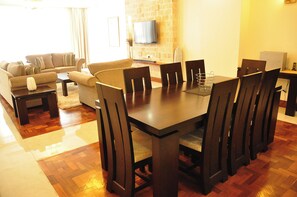 Un comedor con una mesa y sillas de madera, un sofá y un televisor instalado en una pared de ladrillo.