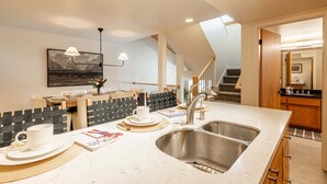 A modern kitchen with a large island, stainless steel sink, and a dining area with a black and white patterned wall. - Newly furnished with private hot tub in Prospector community (Park City)