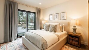 A bedroom with a large bed, two bedside lamps, a window with curtains, and framed pictures on the wall. - Newly furnished with private hot tub in Prospector community (Park City)