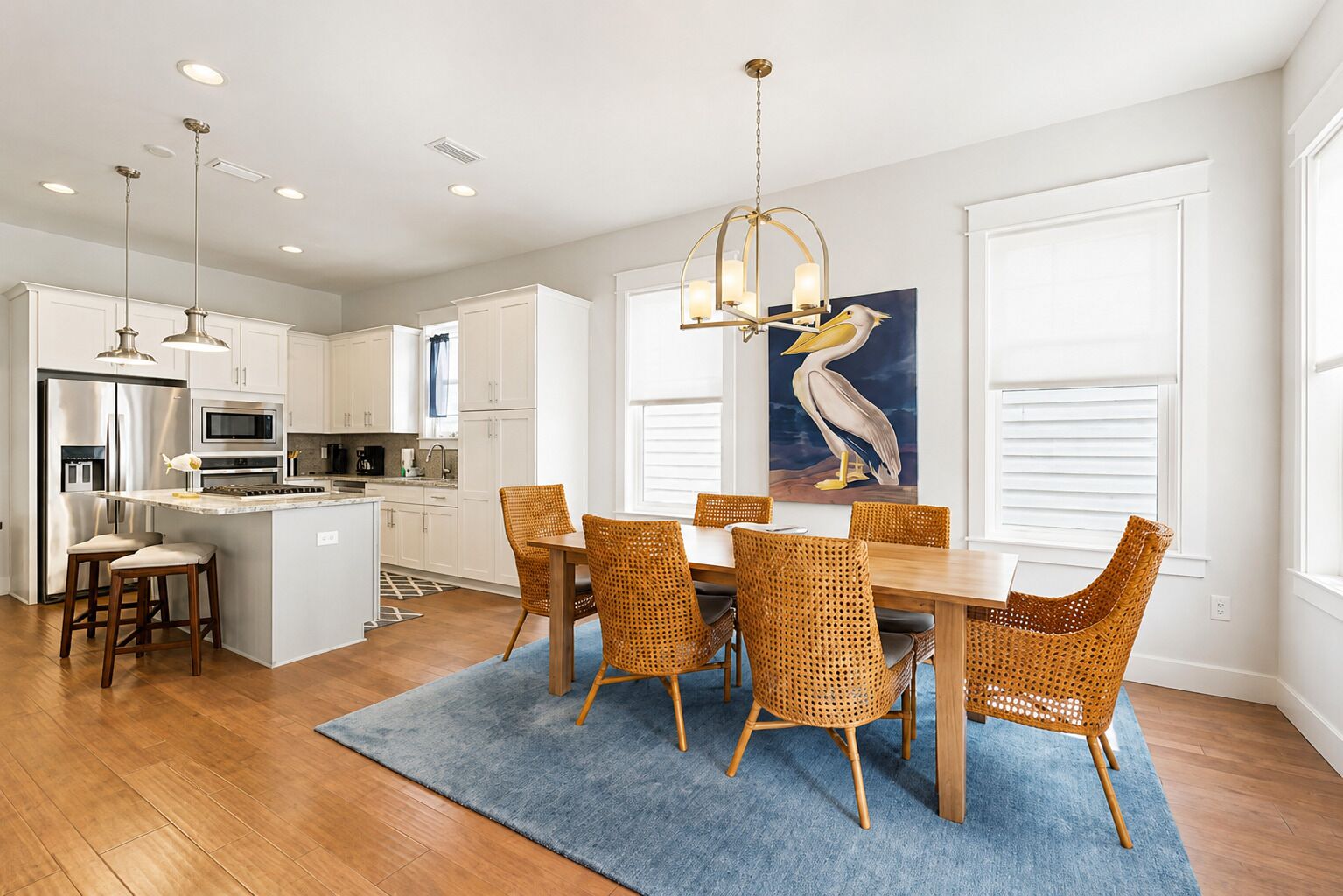 A modern kitchen with white cabinetry, stainless steel appliances, and a dining area with wicker chairs and a blue rug.