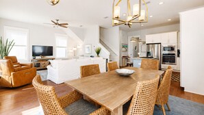 A spacious living room with a large wooden dining table, wicker chairs, a sofa, a TV, and a ceiling fan. - Golf Cart ☀️ 6 Seat Cart thru 10/31, 3 Min to Beach, Foosball, Pool ☀️ Dune Allen (Santa Rosa Beach)