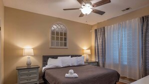A bedroom with a bed, two bedside tables, a ceiling fan, a window, and curtains.