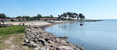 A lakeside area with a rocky shoreline, picnic tables, and a row of cabins in the background.
