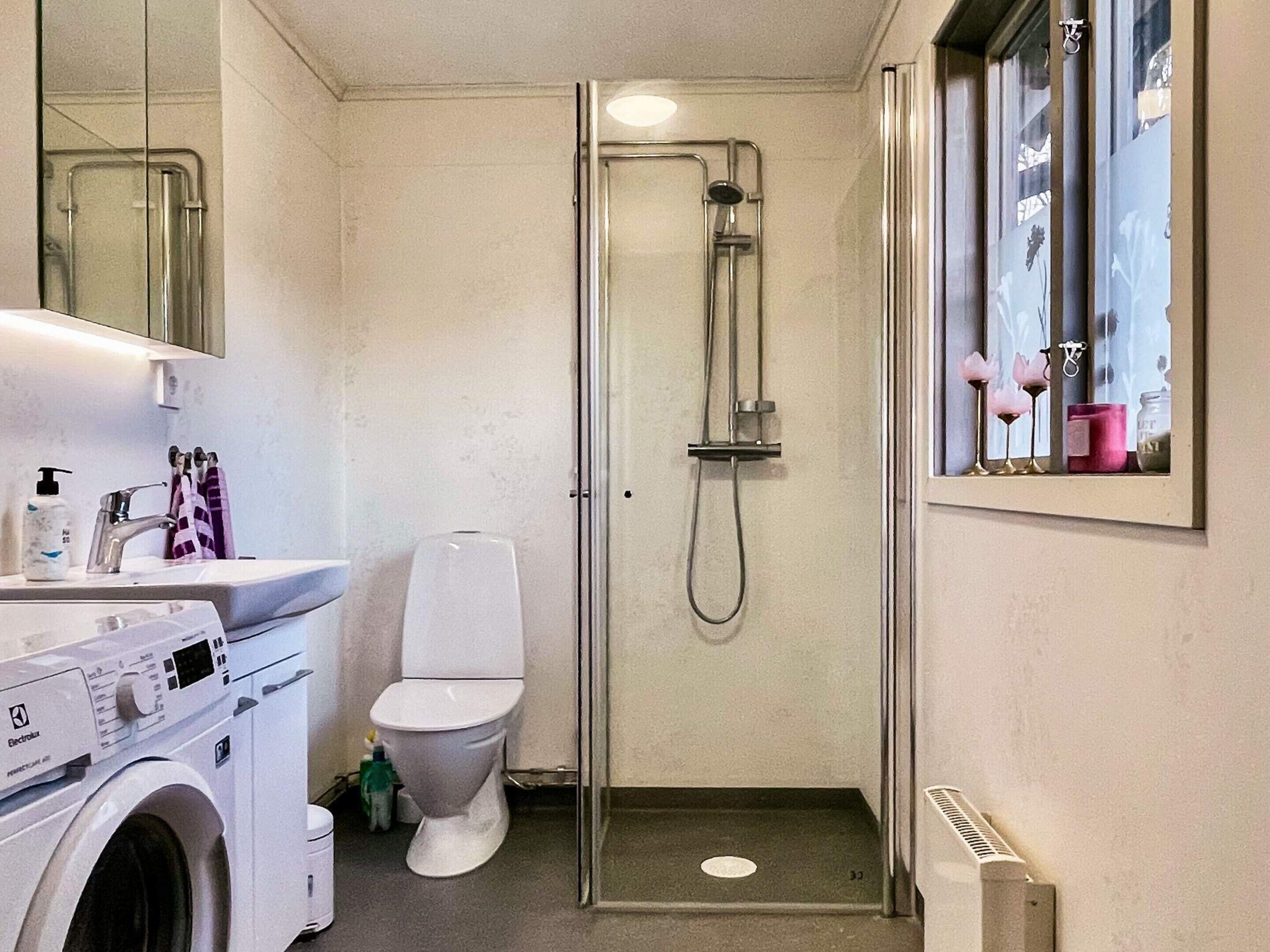Un baño pequeño con lavadora, inodoro y cabina de ducha de cristal.