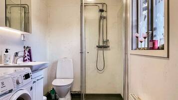 Un baño pequeño con lavadora, inodoro y cabina de ducha de cristal.