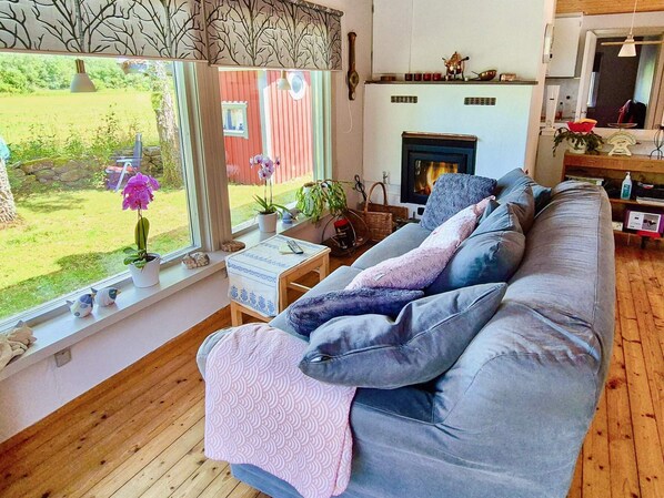 A cozy living room with a sofa, a fireplace, and a view of a garden. - 4 Person Holiday Home in Farjestaden (Farjestaden)