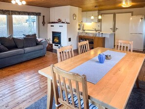 A cozy living room with a sofa, a dining table with chairs, a fireplace, and a kitchen area with cabinets and a refrigerator. - 4 Person Holiday Home in Farjestaden (Farjestaden)