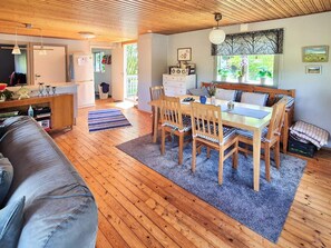A cozy interior with a wooden dining table, chairs, a sofa, and a kitchen area.