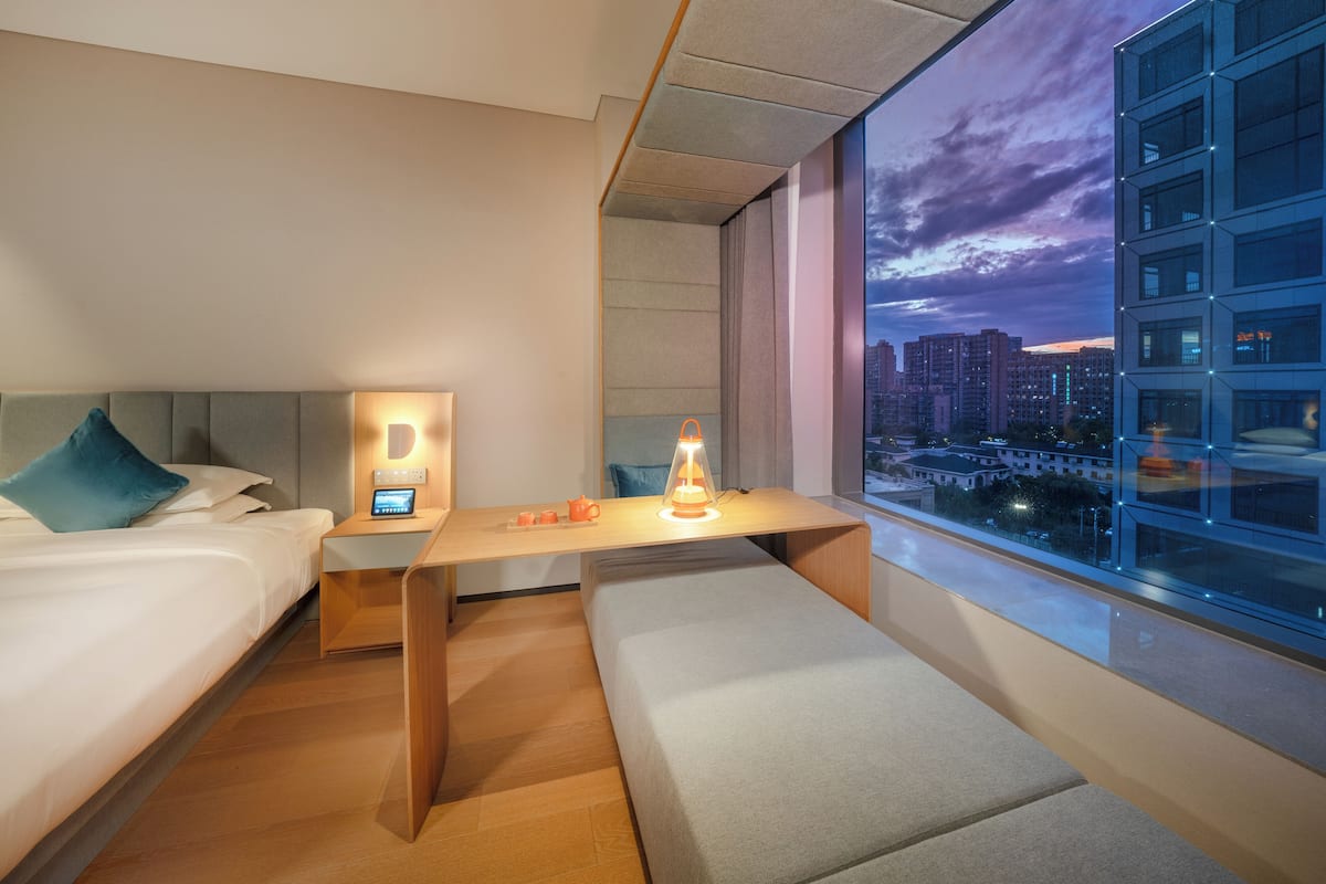 Habitación de hotel moderna con cama, mesita de noche, lámpara y vistas a la ciudad.