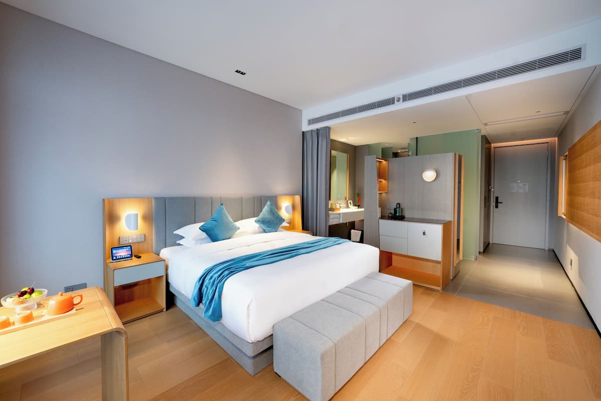 Una habitación de hotel moderna con una cama grande, mesitas de noche, un tocador con espejo y un vestidor.