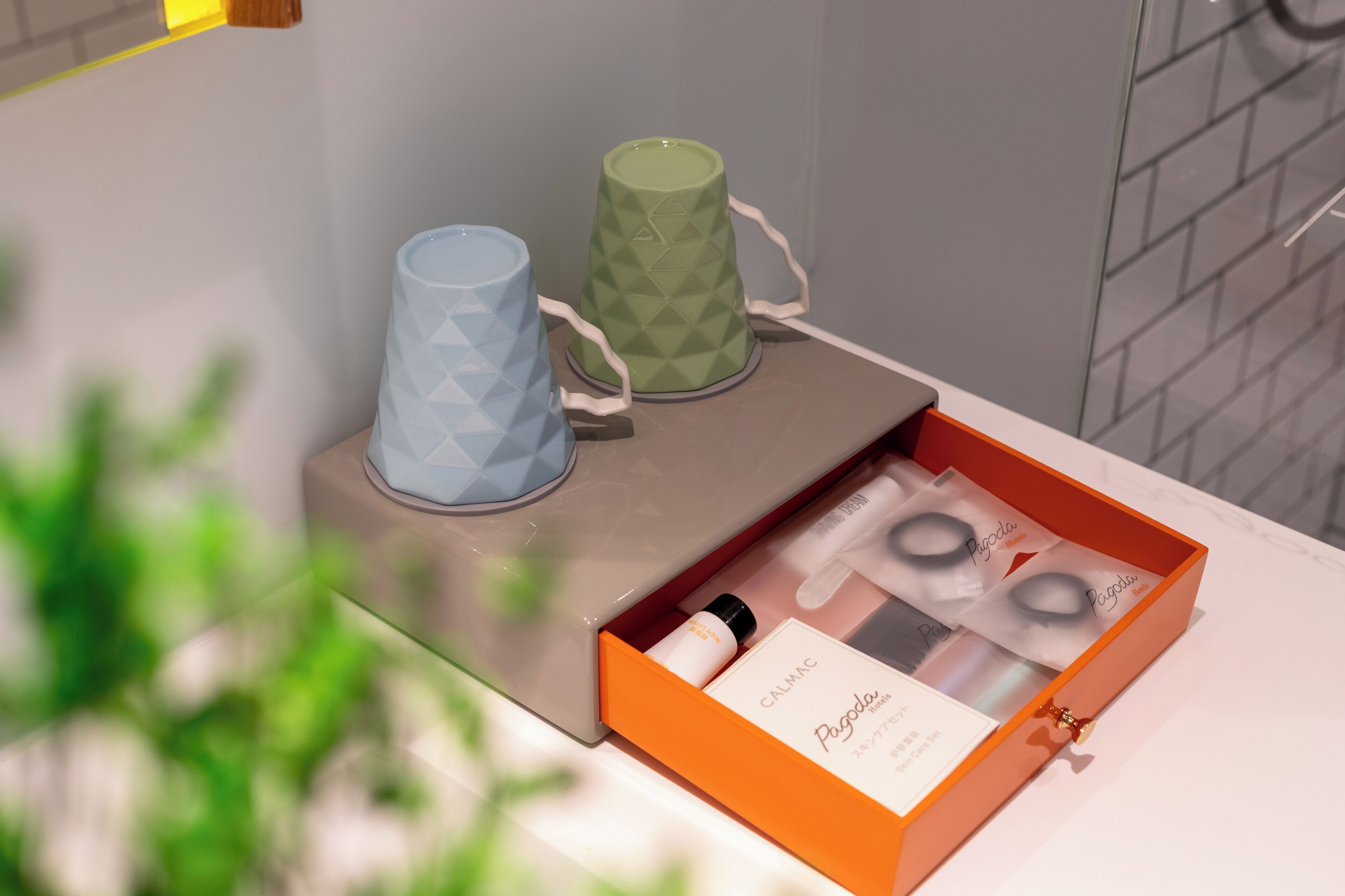 A bathroom with a white countertop, two geometric-patterned candles, and a box containing a bottle and a small item.