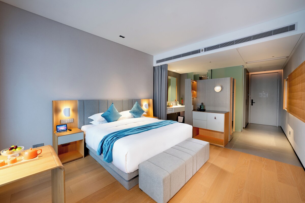 Una habitación de hotel moderna con una cama grande, mesitas de noche, un tocador con espejo y un vestidor.